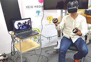 図3 　左：Fusionの操作をしているサライジ氏　右：ロボットハンドで自分を指さす